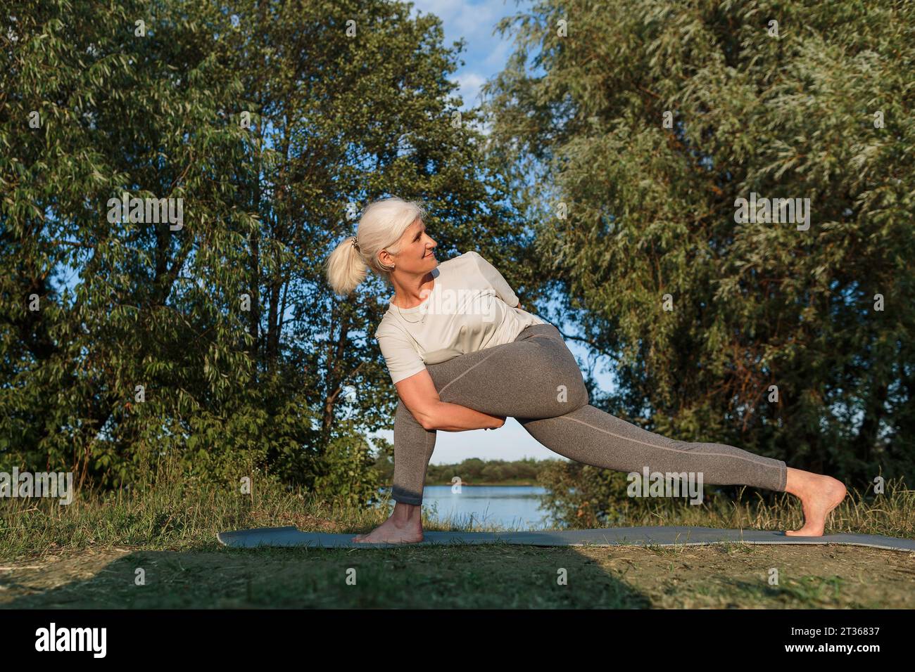 Flexible Frau, die Yoga auf Matte am Seeufer übt Stockfoto