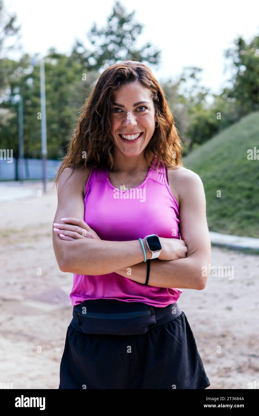 Glückliche Frau, die mit überkreuzten Armen im Park steht Stockfoto