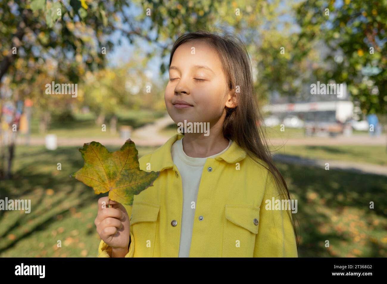 Mädchen mit geschlossenen Augen, das Ahornblatt im Park hält Stockfoto