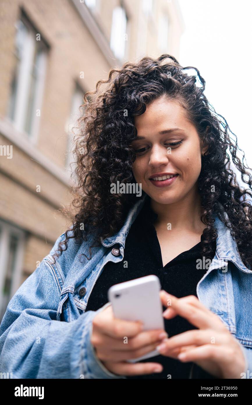 Lächelnde Frau mit lockigen Haaren mit Smartphone Stockfoto
