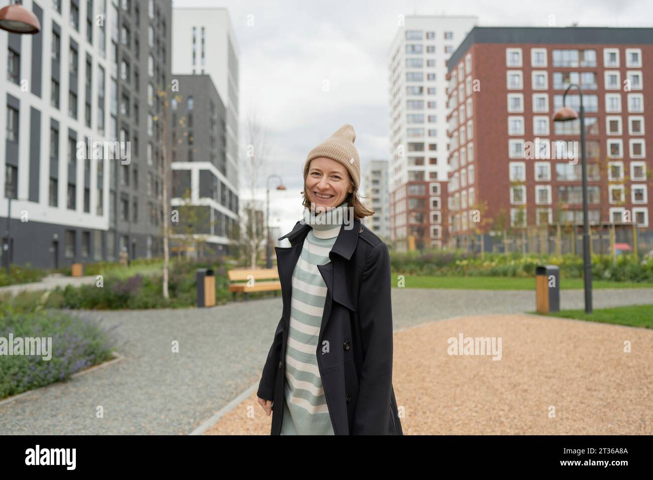 Lächelnde Frau mit Strickmütze und Regenmantel in der Stadt Stockfoto
