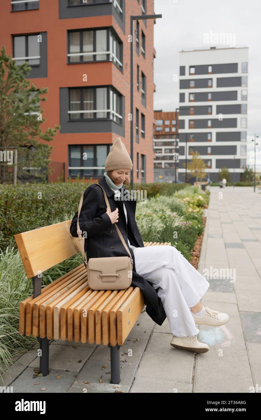 Lächelnde Frau mit Sling Bag, die auf der Parkbank sitzt Stockfoto