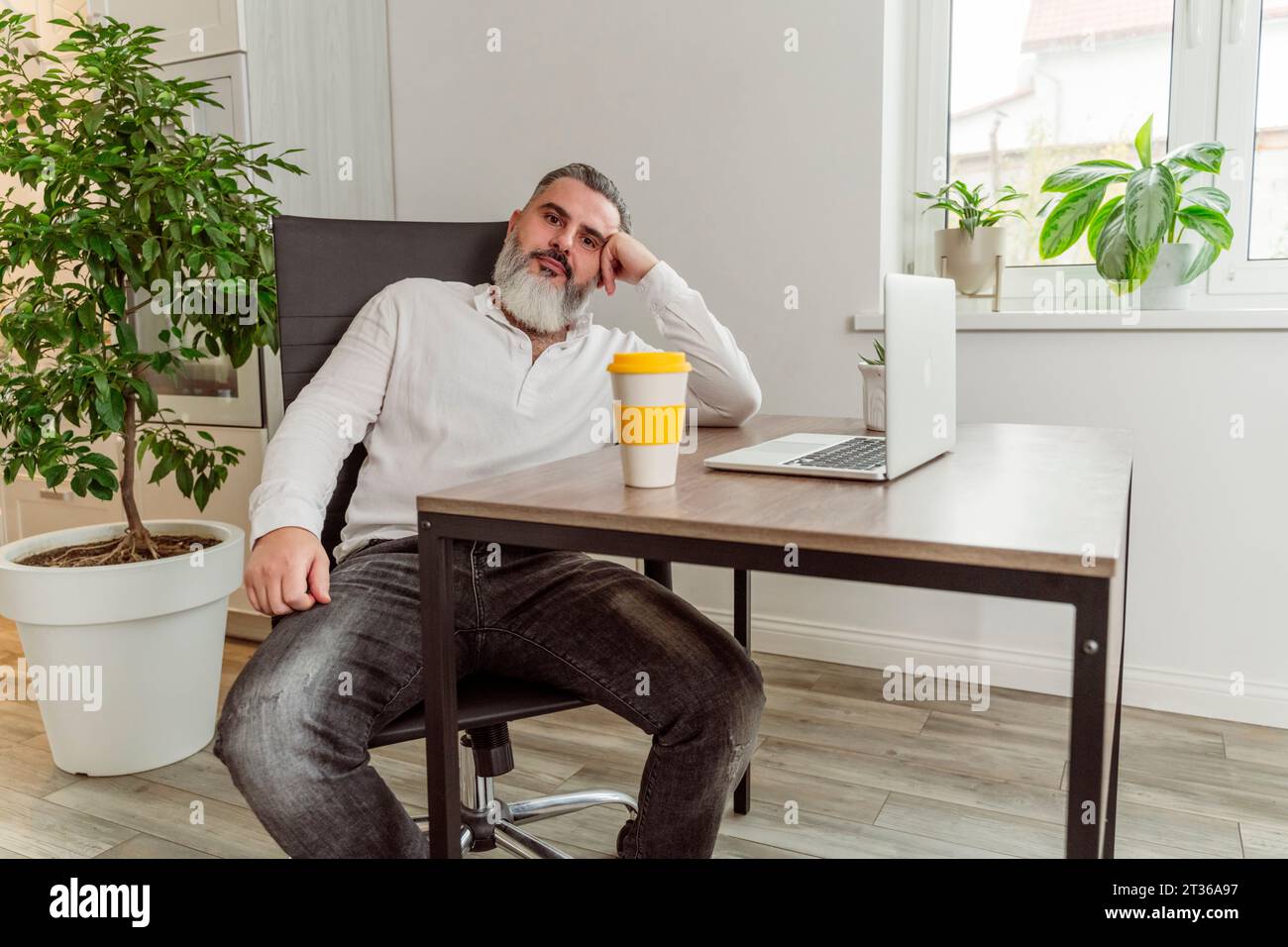Aufmerksamer Geschäftsmann mit wiederverwendbarem Kaffee und Laptop auf dem Tisch am Arbeitsplatz Stockfoto