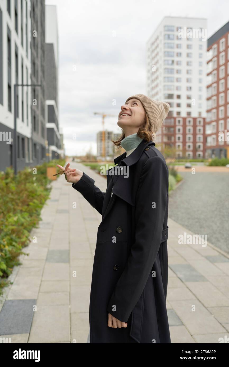Lächelnde Frau, die Schlüssel in der Nähe des Gebäudes hält Stockfoto