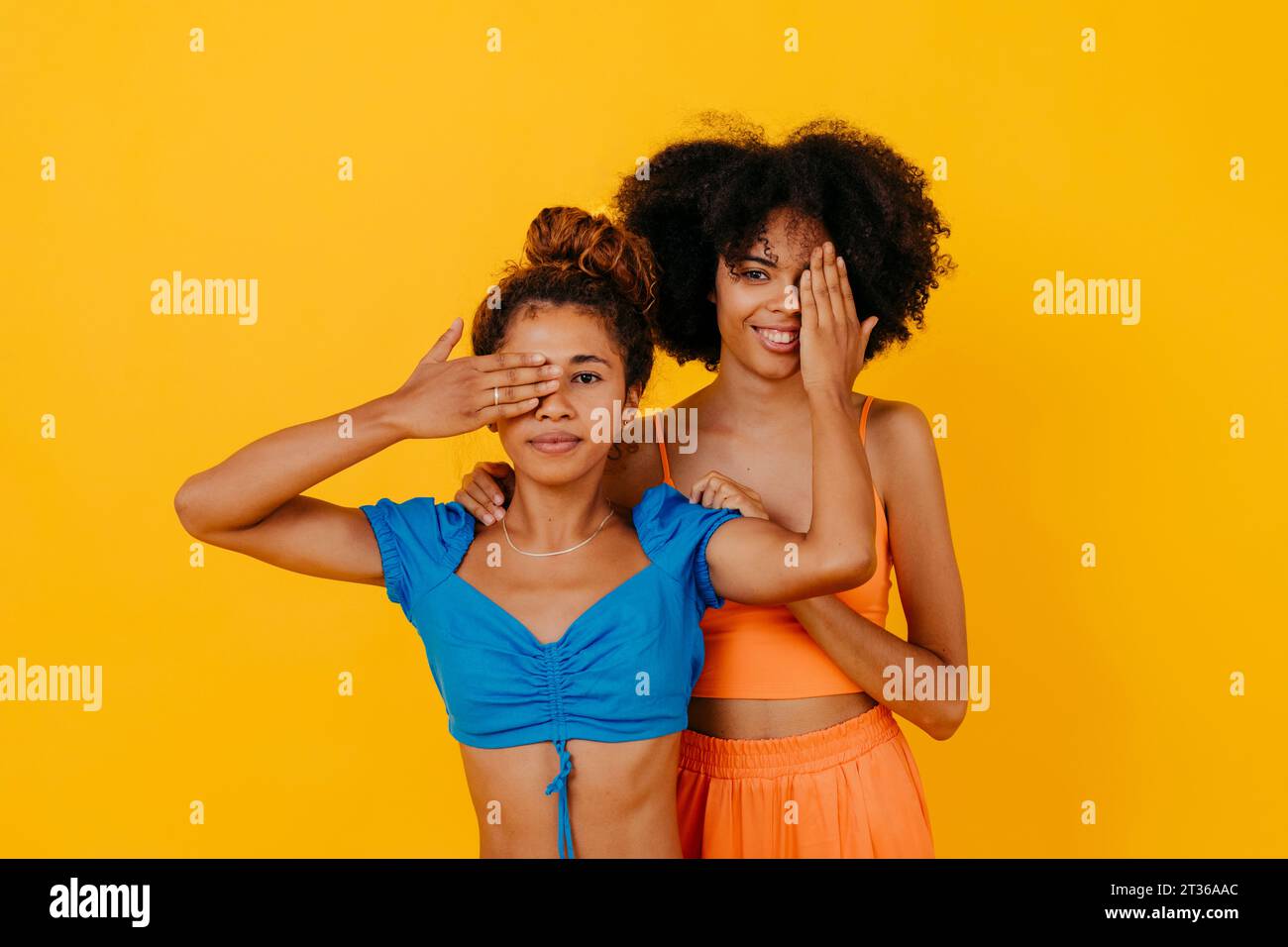 Frau, die ein Auge von sich und Freund vor gelbem Hintergrund bedeckt Stockfoto