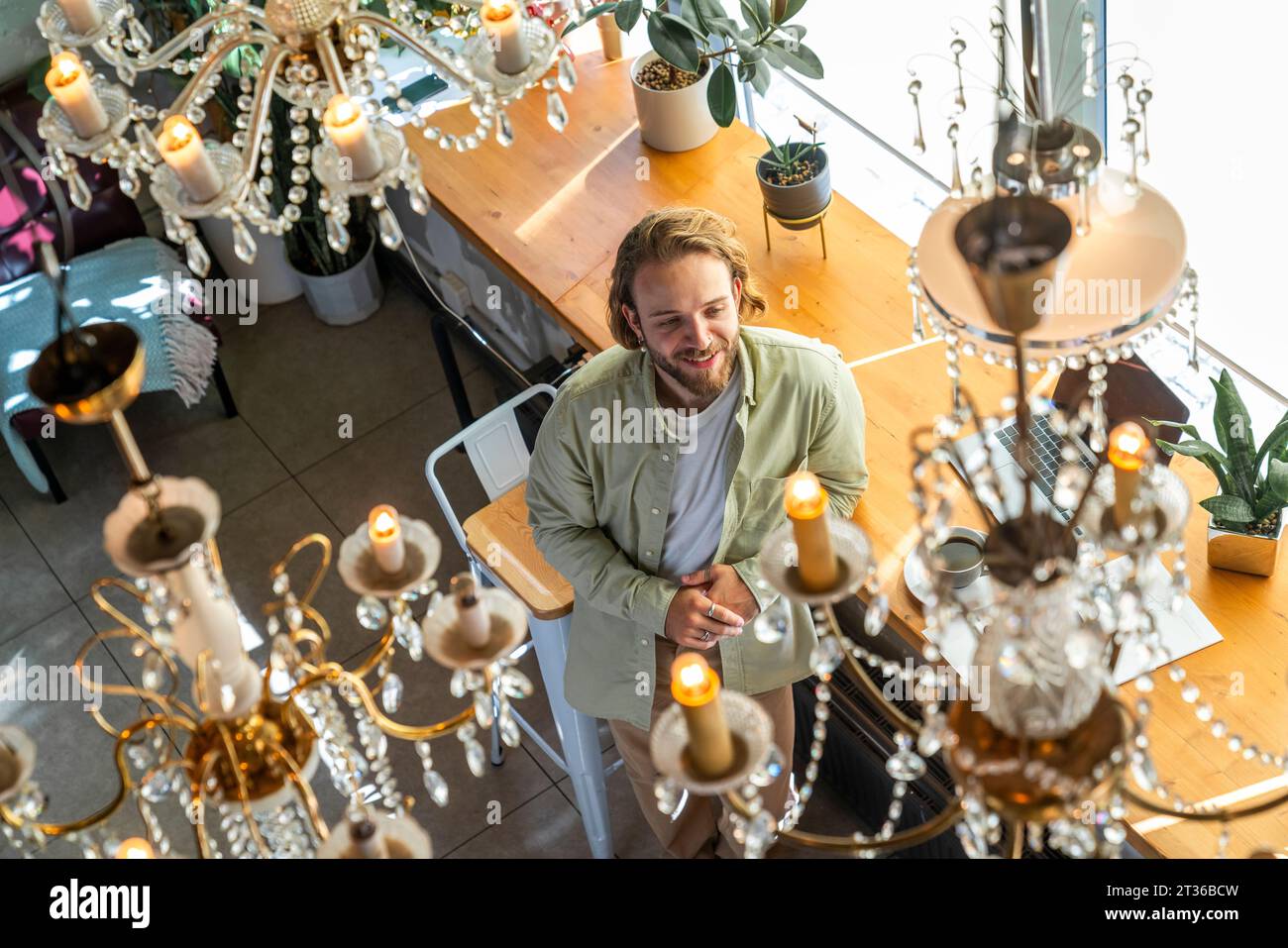 Lächelnder Geschäftsmann, der sich auf den Tisch unter Kronleuchtern im Café lehnt Stockfoto