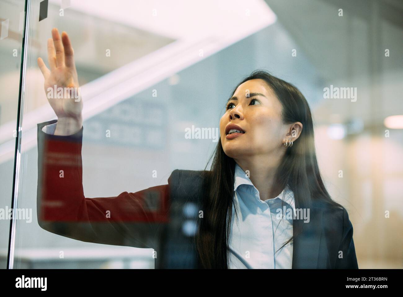Selbstbewusste Geschäftsfrau, die am Arbeitsplatz die Glaswand berührt Stockfoto