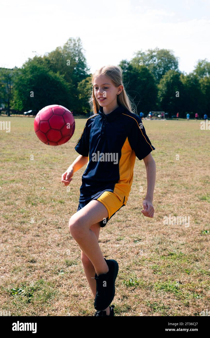 Lächelndes Mädchen, das Fußball auf dem Sportplatz übt Stockfoto