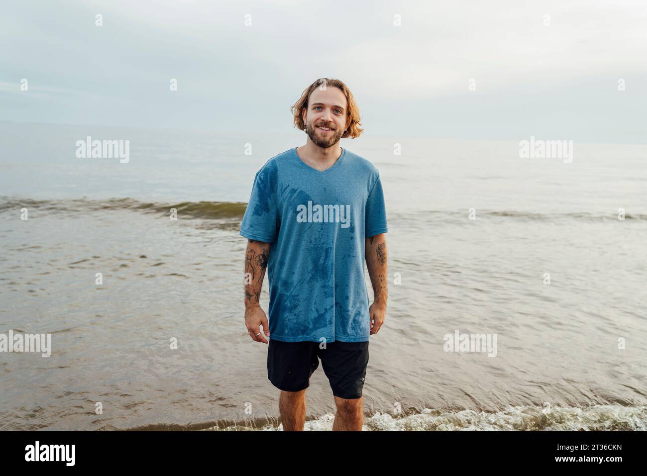 Lächelnder Mann mit T-Shirt in der Nähe des Meeres am Strand Stockfoto