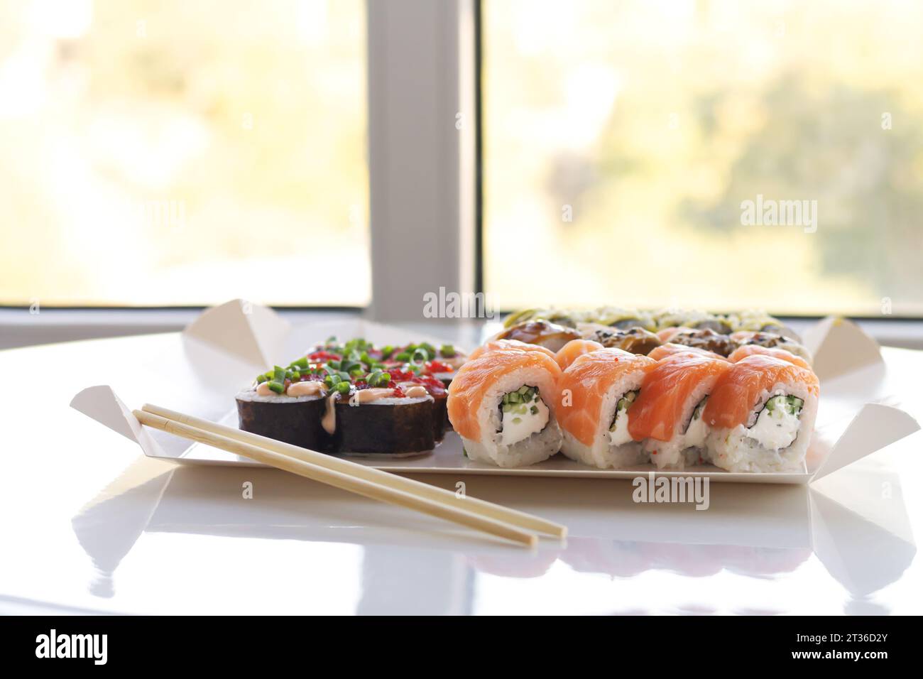 Leckere Sushi-Rollen in Einweg-Papierkarton auf weißem Tisch. Lieferservice Japan Food im Öko-Container-Konzept Stockfoto