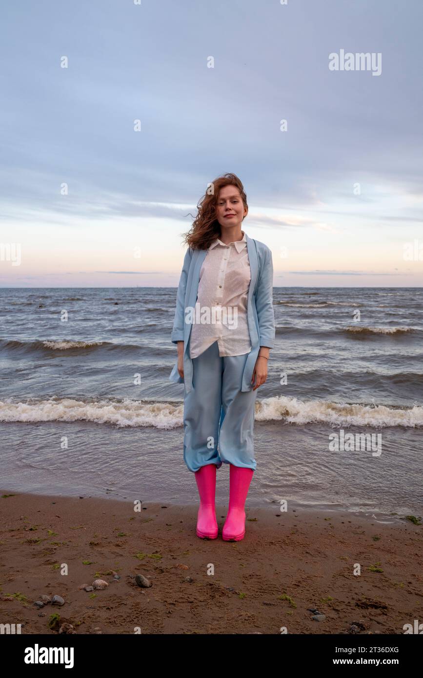 Eine junge Frau mit rosa Gummistiefeln, die am Strand steht Stockfoto