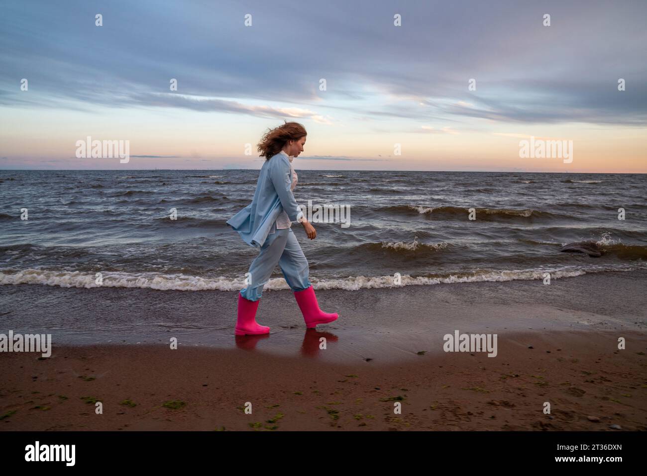 Eine junge Frau, die pinkfarbene Gummistiefel trägt und am Strand läuft Stockfoto