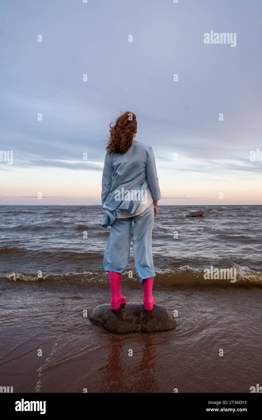 Eine junge Frau mit rosa Gummistiefeln, die am Strand auf Felsen steht Stockfoto