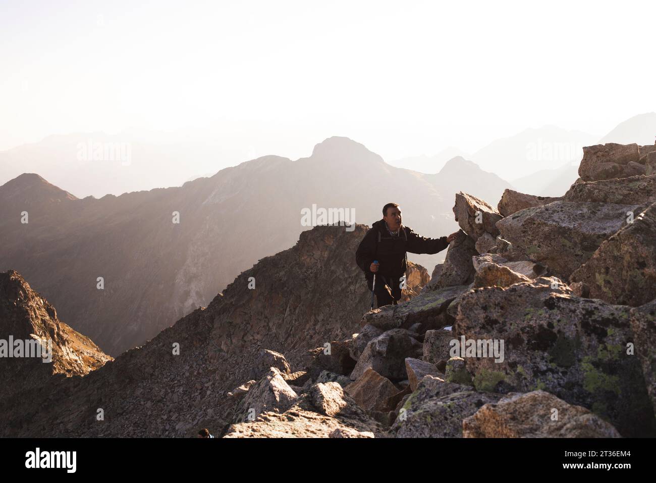 Reifer Mann, der bei Sonnenaufgang auf felsigem Berg wandert Stockfoto