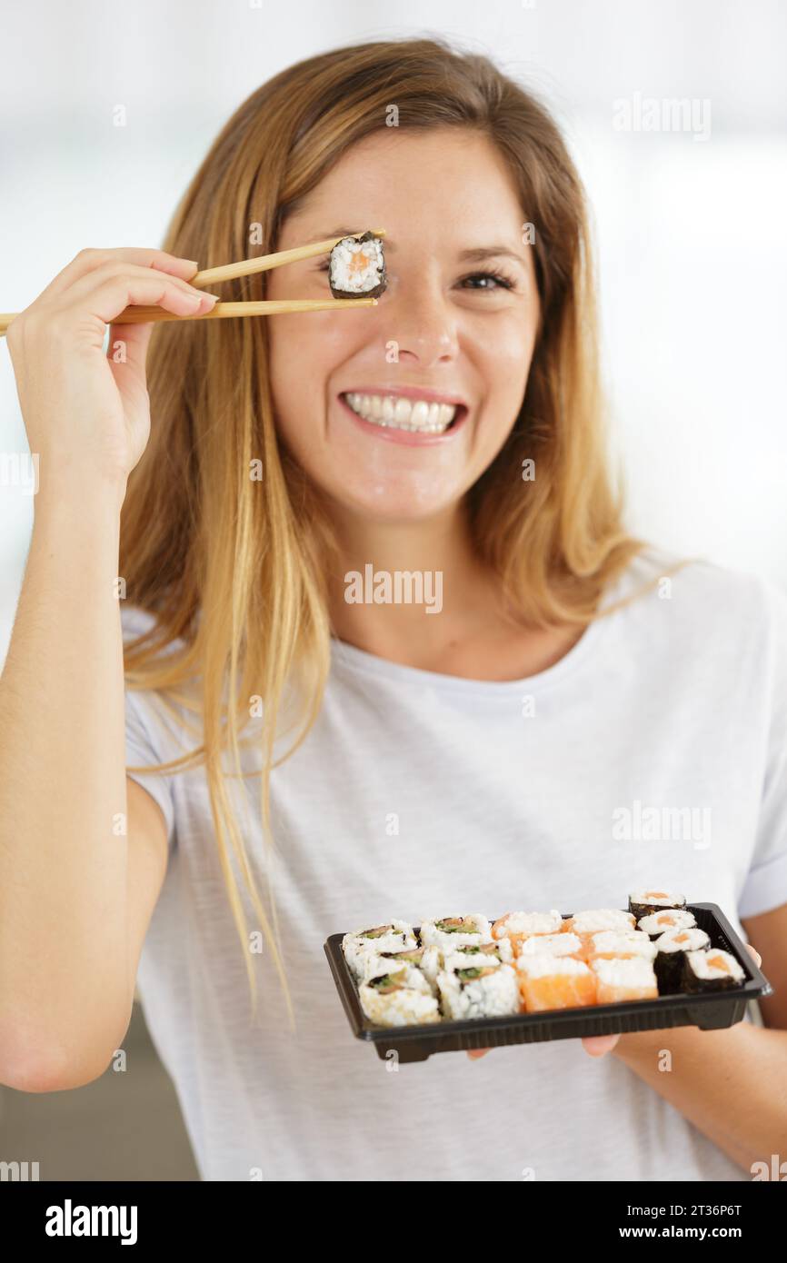 Eine verspielte junge Frau, die eine Sushi-Rolle hält Stockfoto