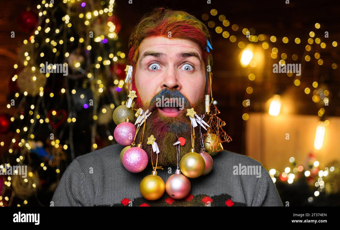 Frohe Weihnachten und frohes neues Jahr. Überraschter bärtiger Mann mit gefärbten Haaren und verziertem Bart mit Weihnachtskugeln. Neujahrsfeier. Weihnachten oder Neu Stockfoto