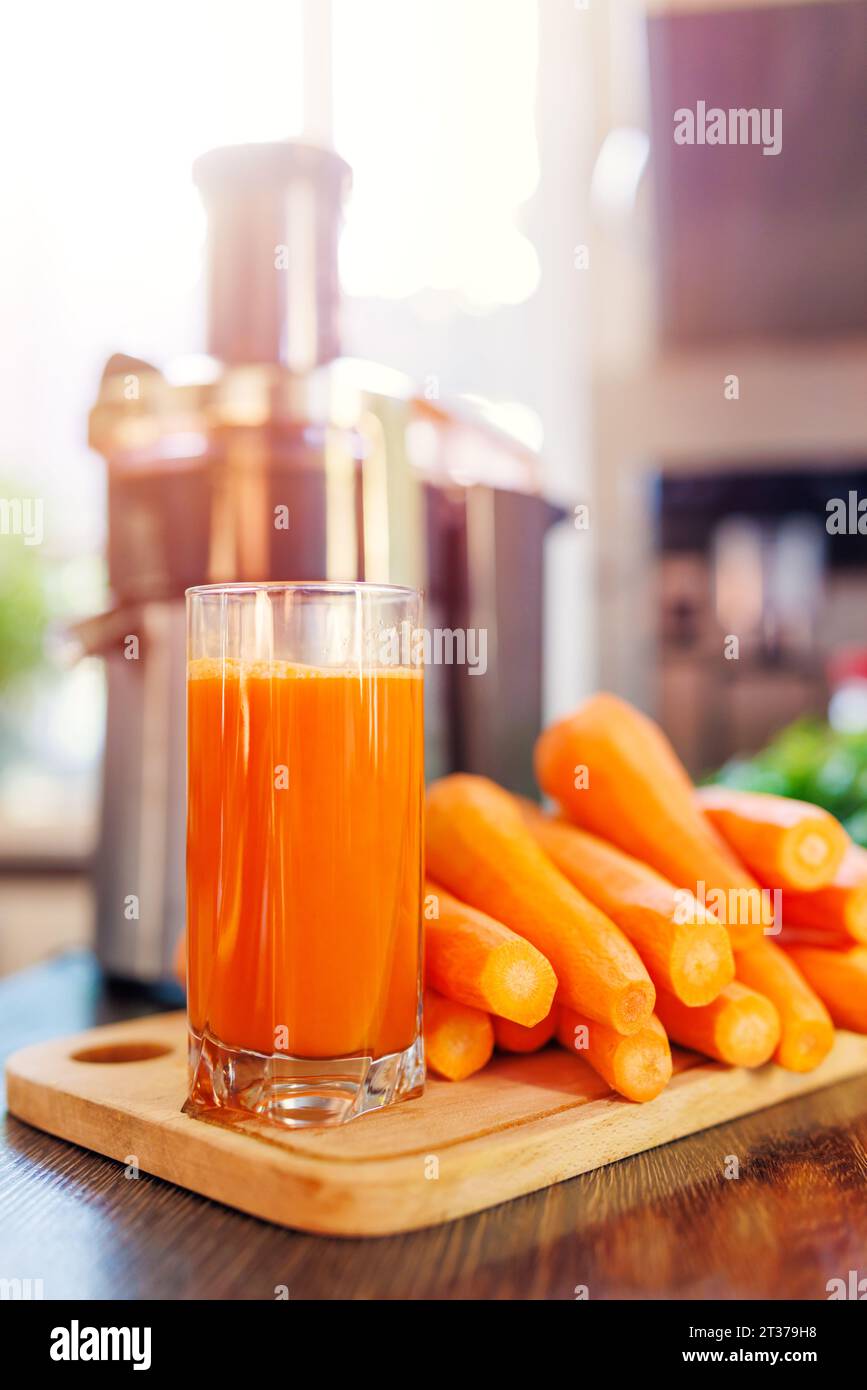 Ein Glas frisch gepressten Karottensaft, Karotten und Saftpresse in der Küche Stockfoto