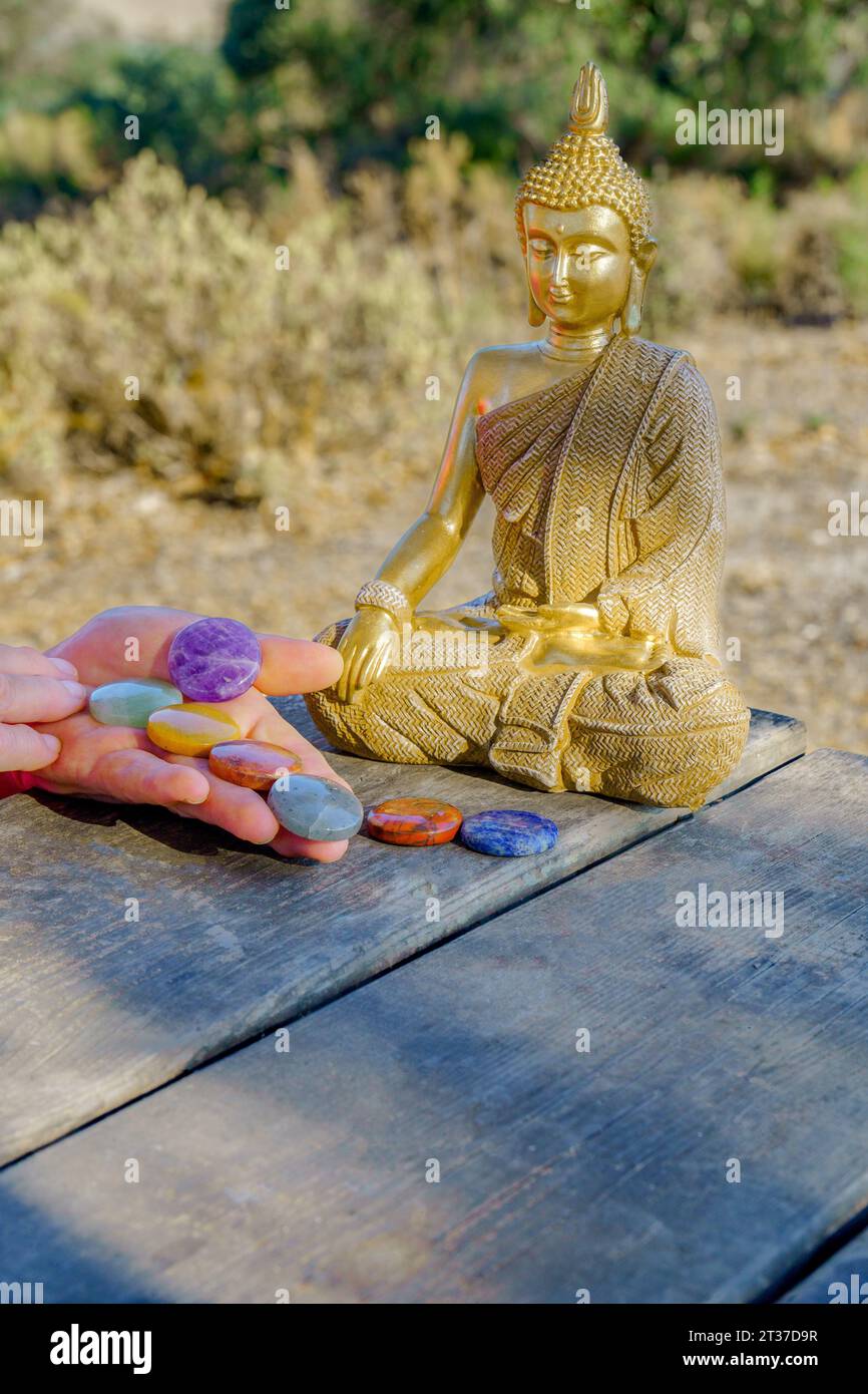 Frauenhände mit Chakra-Steinen auf einem Holztisch mit einer buddha-Statue im Hintergrund Stockfoto