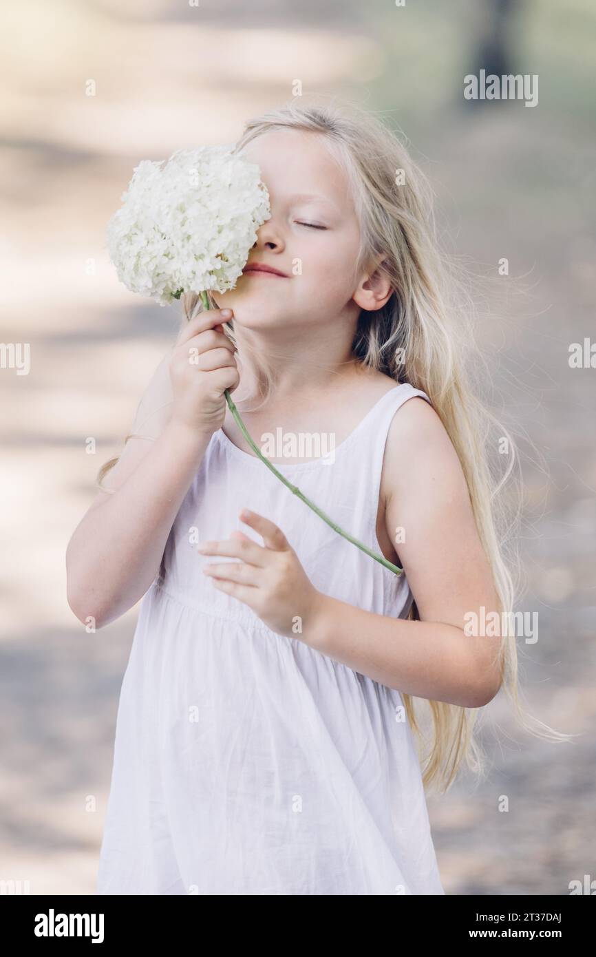 Porträt eines jungen, schönen Mädchens, das einen Teil ihres Gesichts hinter einer Hortensie versteckt und lächelt. Vertikaler Rahmen. Stockfoto