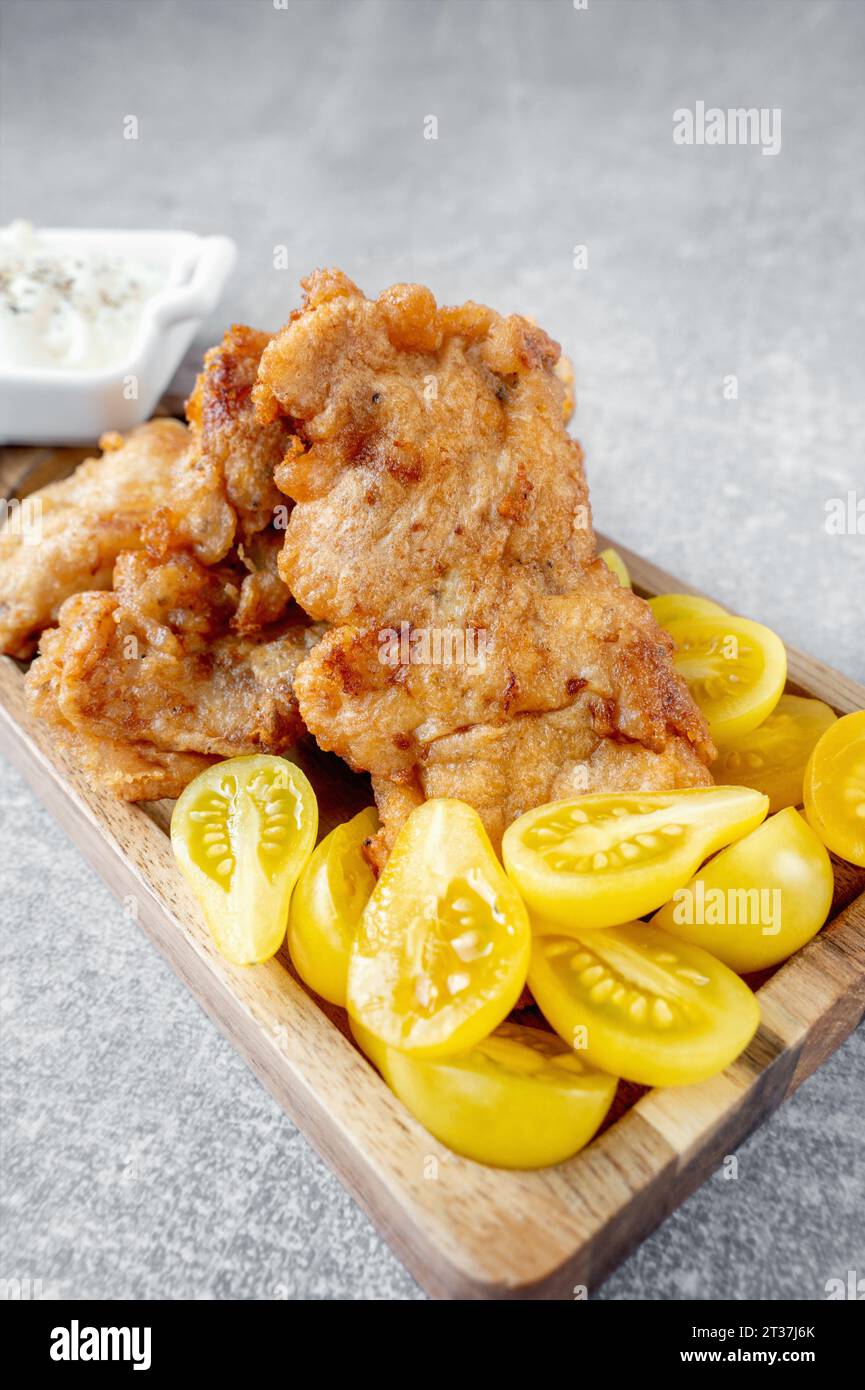 Das Fischgericht besteht aus gebratenem Kabeljaufilet mit einer cremigen Sauce und gelben Pflaumentomaten, serviert auf einer fischförmigen Holzplatte. Kopierbereich Stockfoto