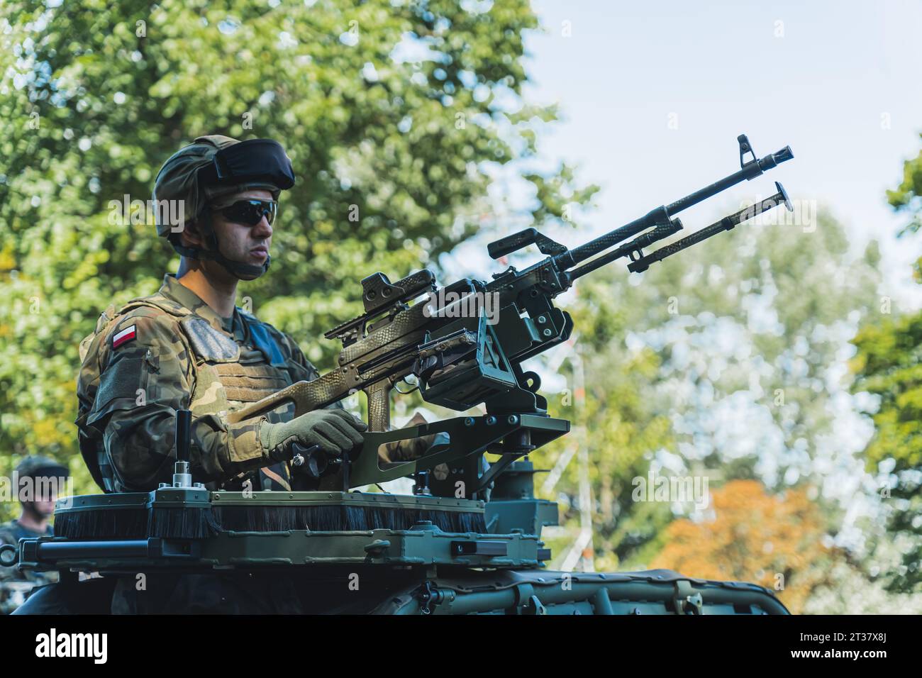 16.08.2023 Warschau, Polen. Moderne militärische Ausrüstung. Polnischer Soldat, der Maschinengewehr hält, während er in der Luke des Kommandanten gegen Bäume steht. Hochwertige Fotos Stockfoto