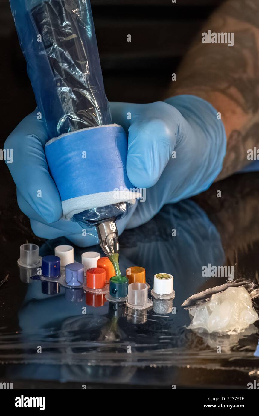 Mit Handschuhen des Tätowierers taucht die Nadel in grüne Farbe. Stockfoto