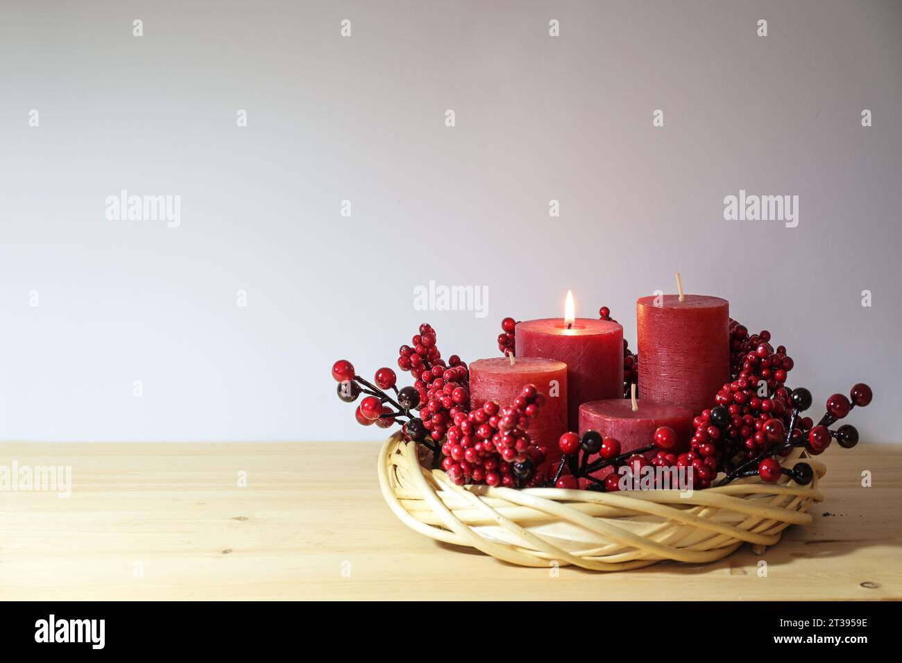 Erster Advent mit vier roten Kerzen, eine davon beleuchtet, in einem natürlichen Weidenkornkranz mit Beerendekoration, saisonaler Wohnkultur, Kopierraum, Sell Stockfoto