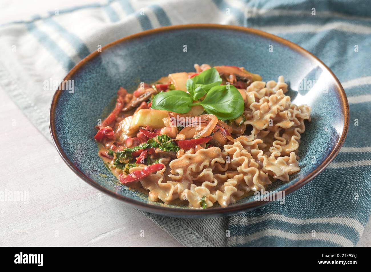 Vollkorn-Dinkelnudeln mit Gemüse in Tomatensauce und Basilikum garnieren in einer blauen Platte, gesundes vegetarisches Gericht, ausgewählte Fokussierung, enge Tiefe des Falles Stockfoto