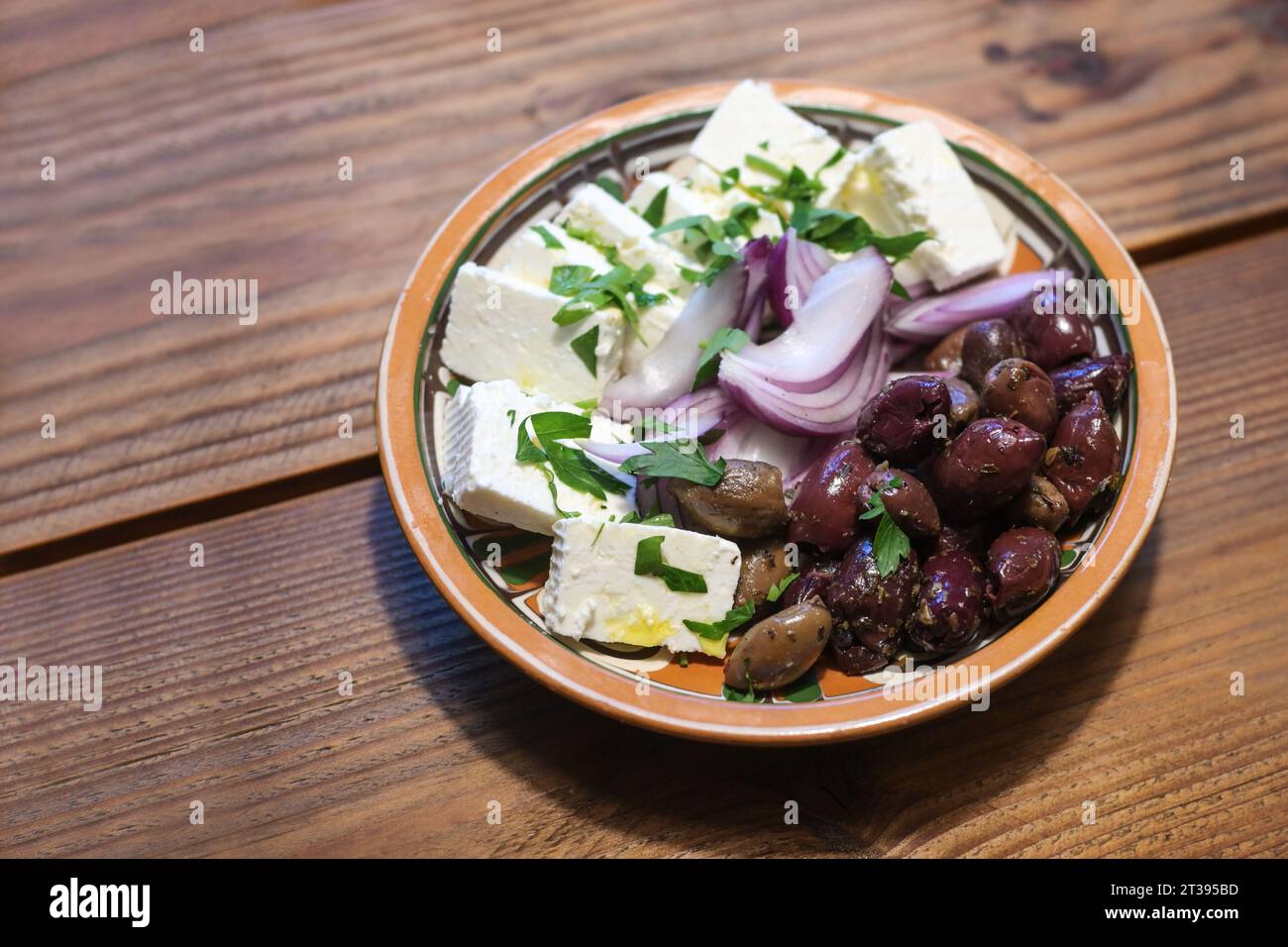 Griechische Vorspeisen, Kräuteroliven, Zwiebeln und Fetakäse in einer Keramikschale auf einem rustikalen Holztisch, Kopierraum, ausgewählter Fokus, enge Tiefe des fixes Stockfoto