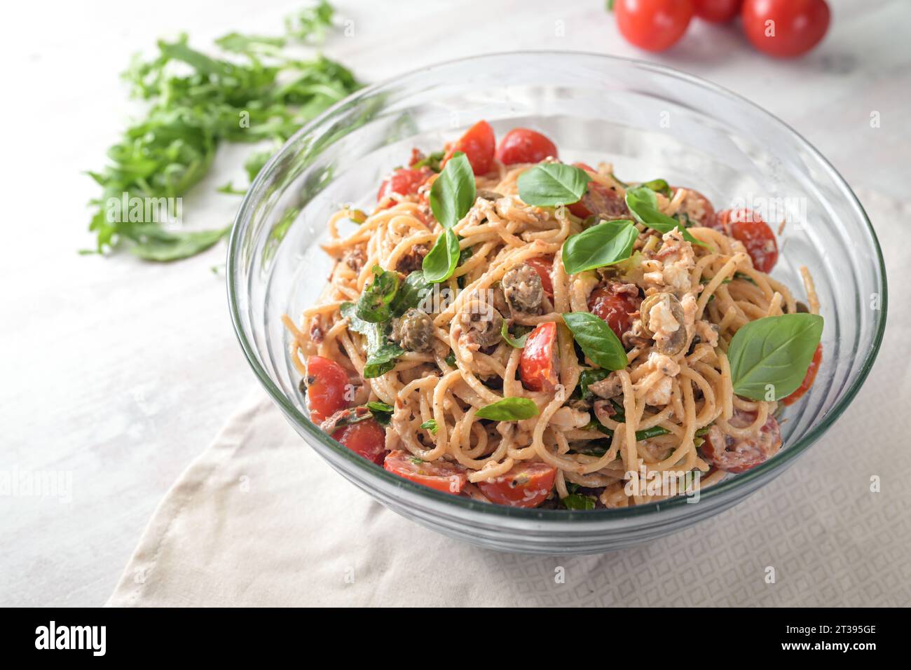 Mediterraner Partysalat aus Spaghetti mit Tomaten, Rucola, Mozzarella, Oliven und Basilikum in einer Glasschale auf einem weiß bemalten Tisch, Kopierraum, Sell Stockfoto