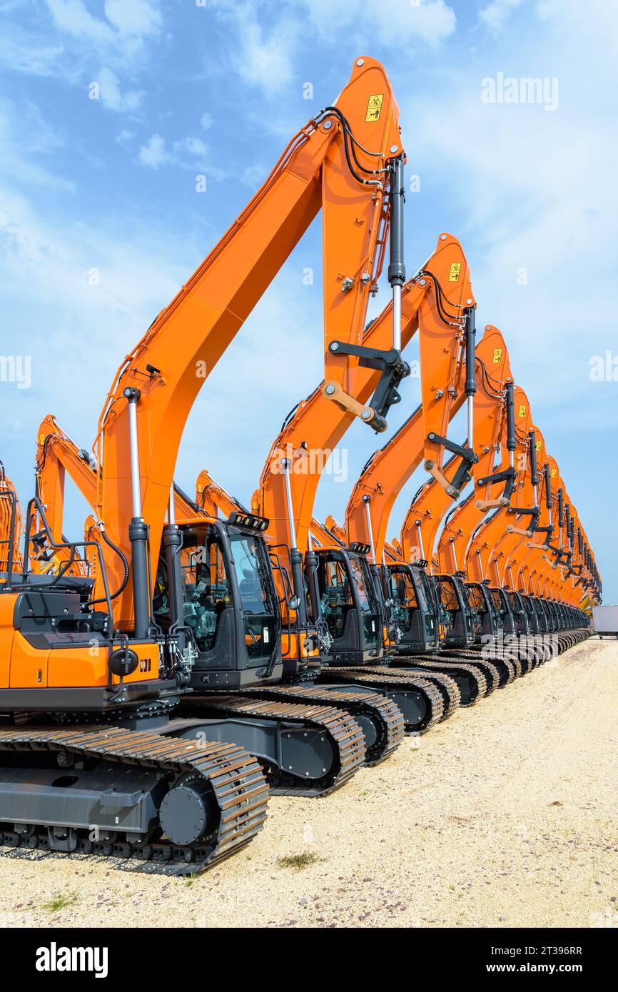 Dutzende brandneuer orangefarbener caterpillar-Hydraulikbagger reihten im Freien unter stürmischem Himmel in einer Reihe an. Stockfoto
