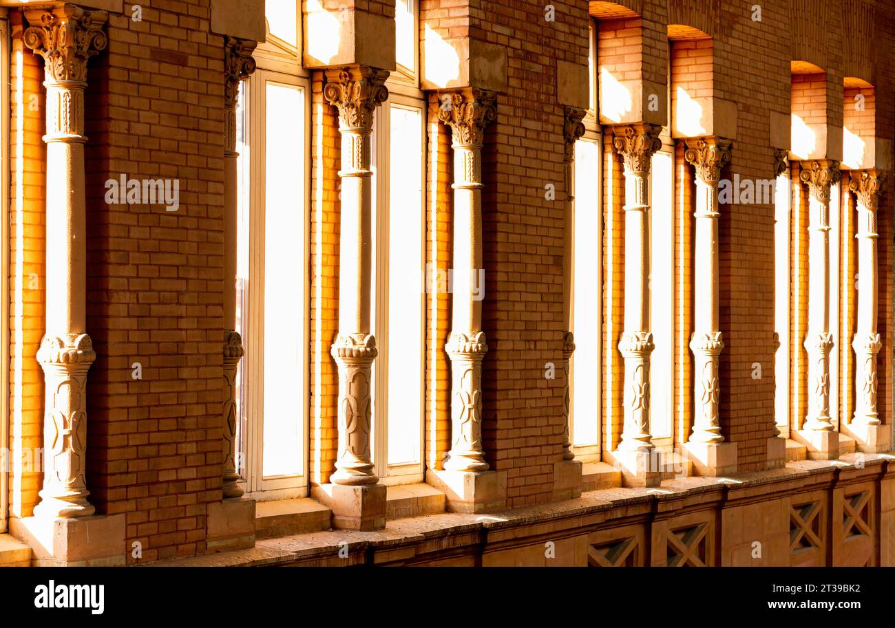 Ziegelmauer mit Fenstern, die mit Säulen geschmückt sind, durch die Sonnenlicht eindringt. Detail des Innenraums des Bahnhofs Atocha, Madrid Stockfoto