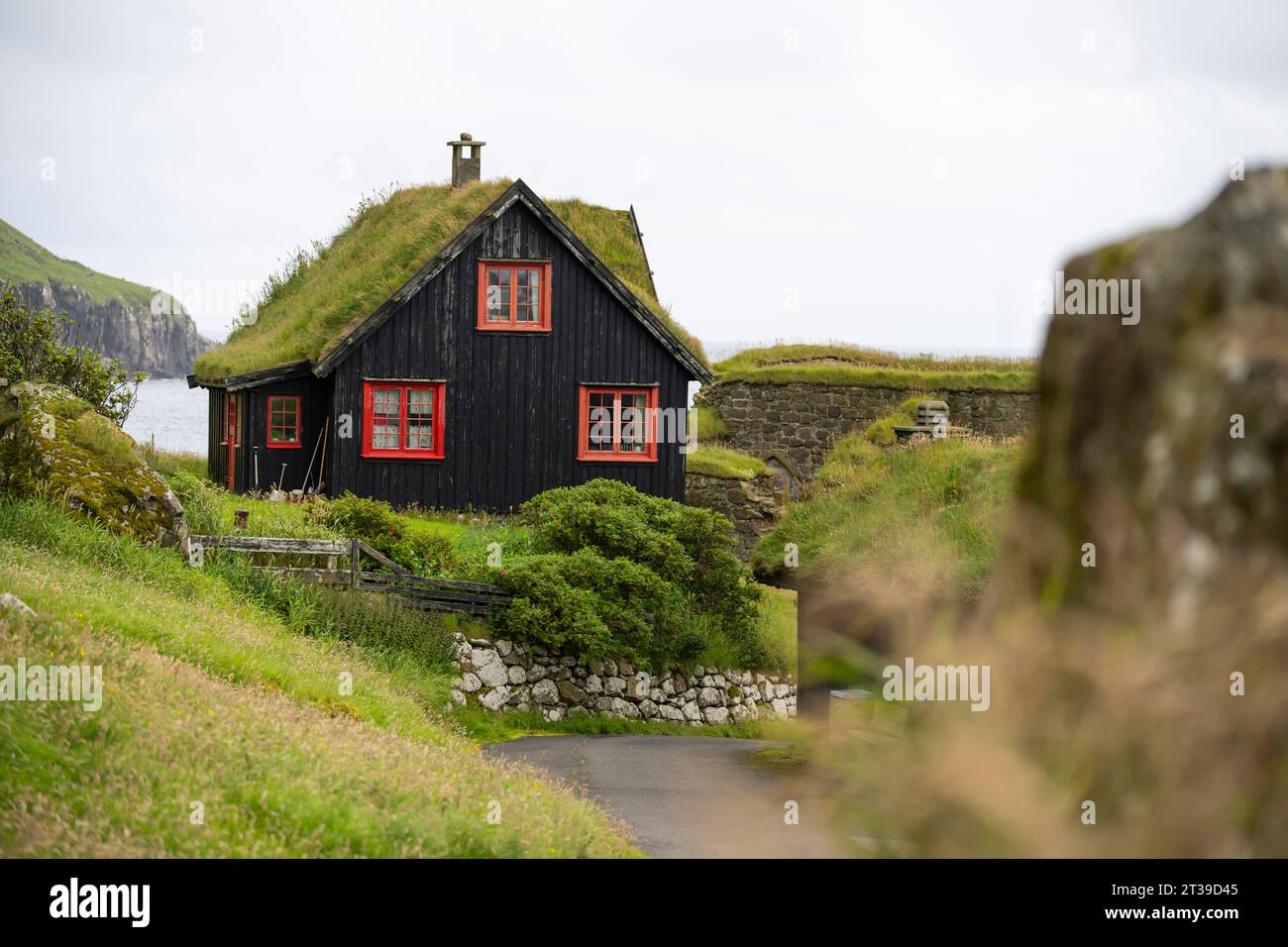 Wohnhaus mit grasbewachsenem Dach auf grünem Gelände mit grünen Bäumen auf den Färöern bei bewölktem Wetter Stockfoto