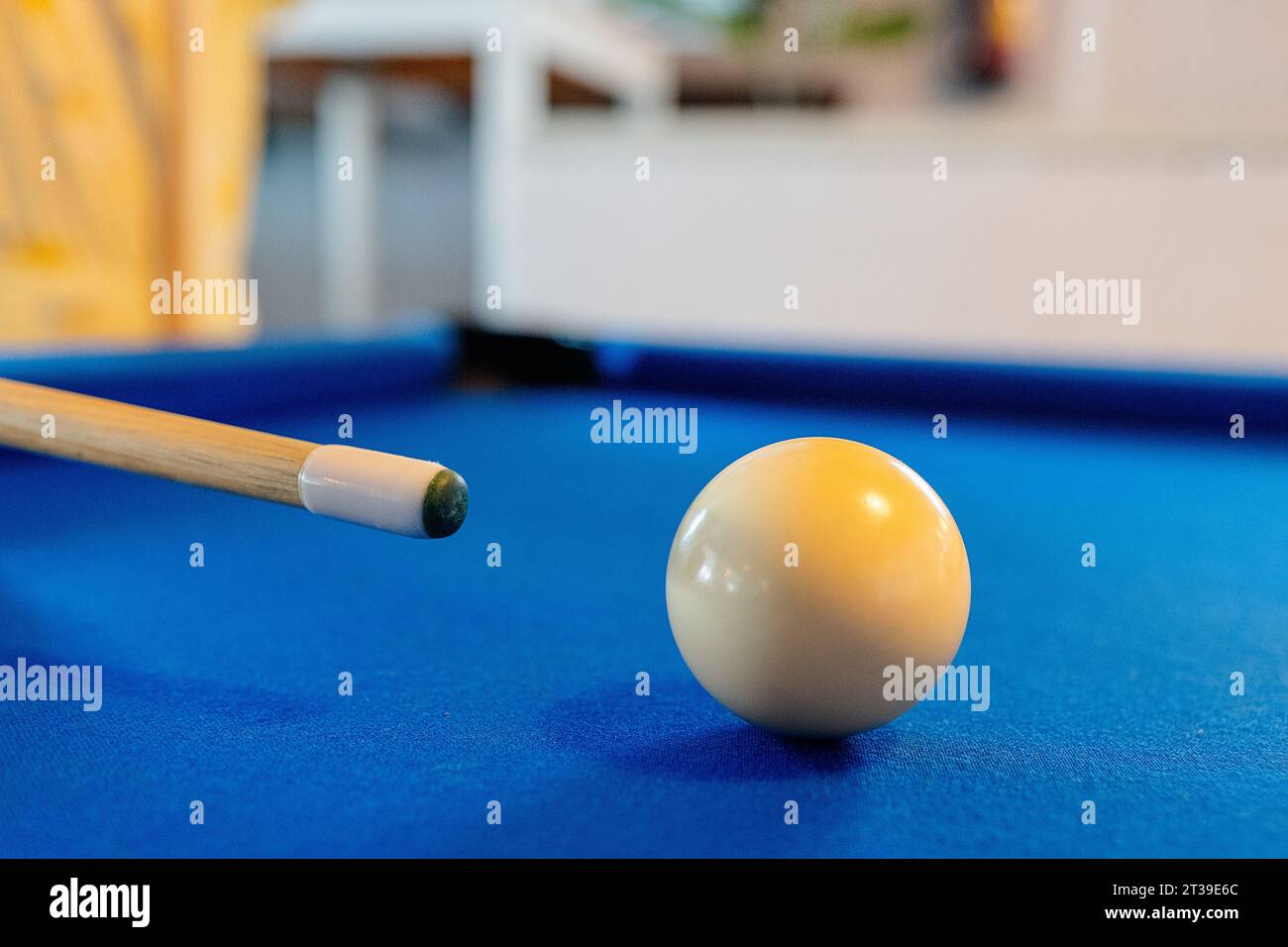 Nahaufnahme einer weißen Billardkugel auf blauem Billardtisch in der Nähe von Cue vor verschwommenem Hintergrund in der Bar Stockfoto
