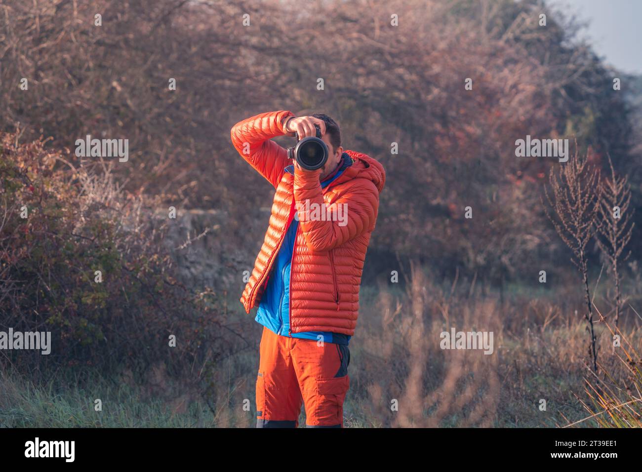 Mann, der ein Foto macht und in die Kamera schaut, während er orange warme Kleidung auf dem Berg trägt Stockfoto