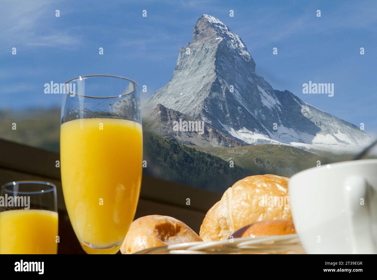 Eine erfrischende Morgenszene mit einem Glas Orangensaft und Gebäck vor der majestätischen Kulisse des Matterhorns unter einem klaren blauen Himmel Stockfoto