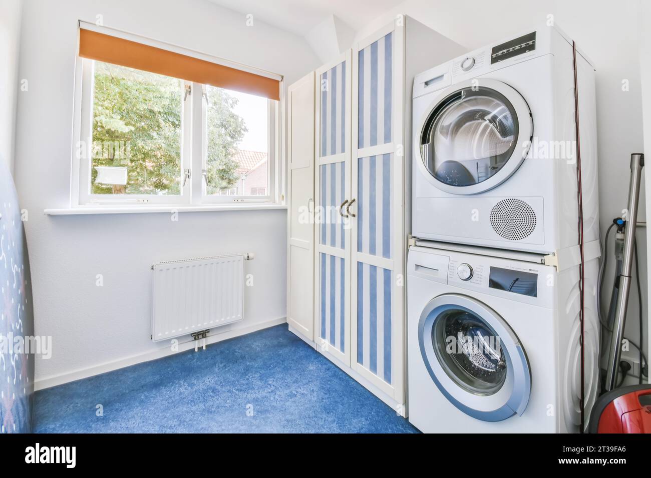 Waschmaschinen und Trockner mit Holzschrank am Fenster im weißen Waschraum des modernen Apartments Stockfoto