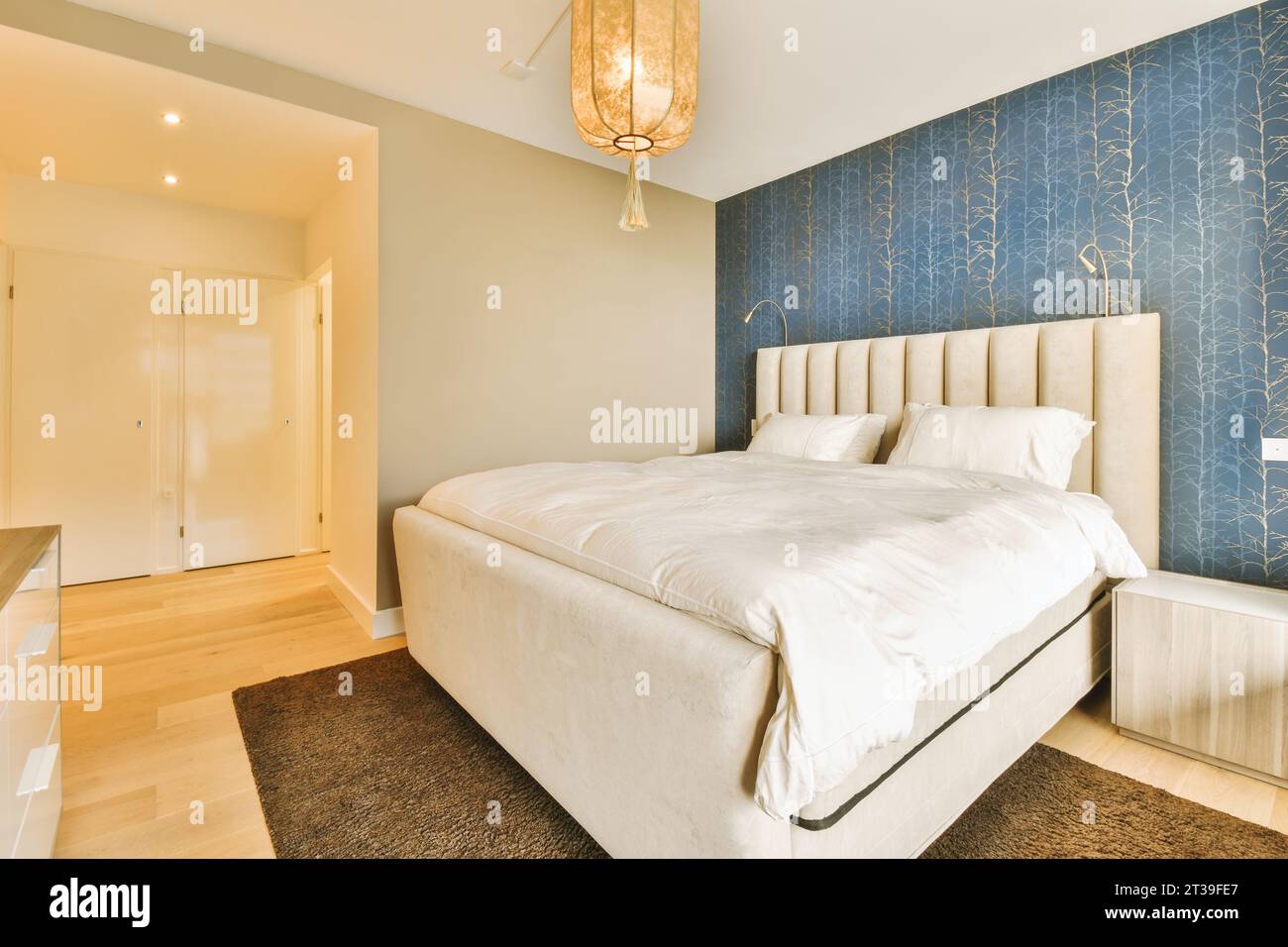 Weißes, gemütliches Bett mit Kissen und Federdecken mit blauer Tapete in einem geräumigen, luxuriösen Schlafzimmer in einem modernen Apartment Stockfoto