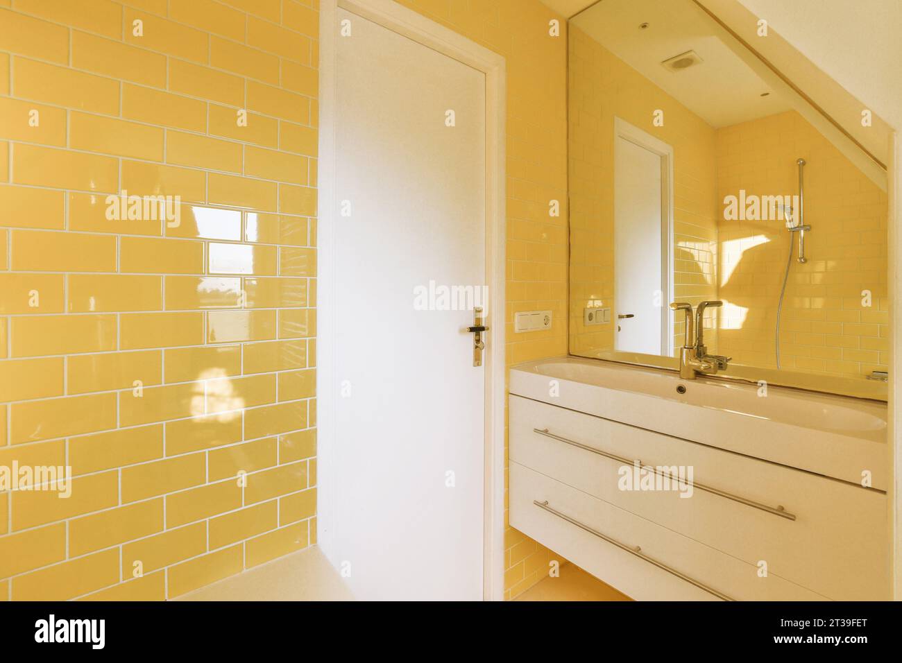 Spiegel mit weißem Keramikwaschbecken durch geschlossene Tür im modernen Badezimmer mit gelben Fliesenwänden in einem modernen Apartment Stockfoto