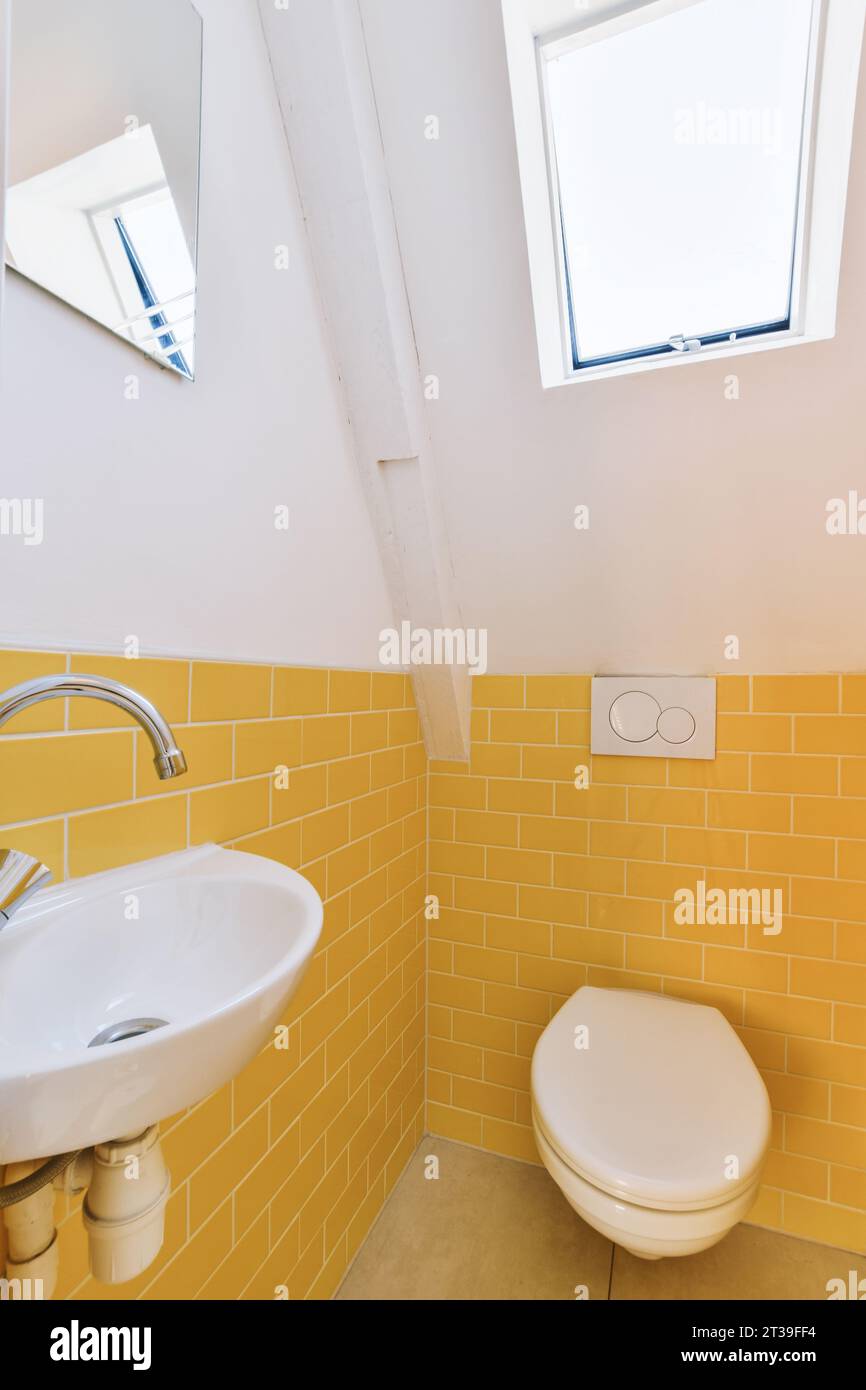 Innenraum eines kleinen Badezimmers mit Keramikwaschbecken und Toilettenschüssel und gelb gefliesten Wänden in einem modernen Apartment Stockfoto