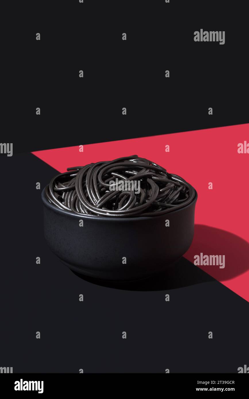 Schwarze Spaghetti in einer Schüssel auf schwarzer und roter Oberfläche an der schwarzen Wand Stockfoto