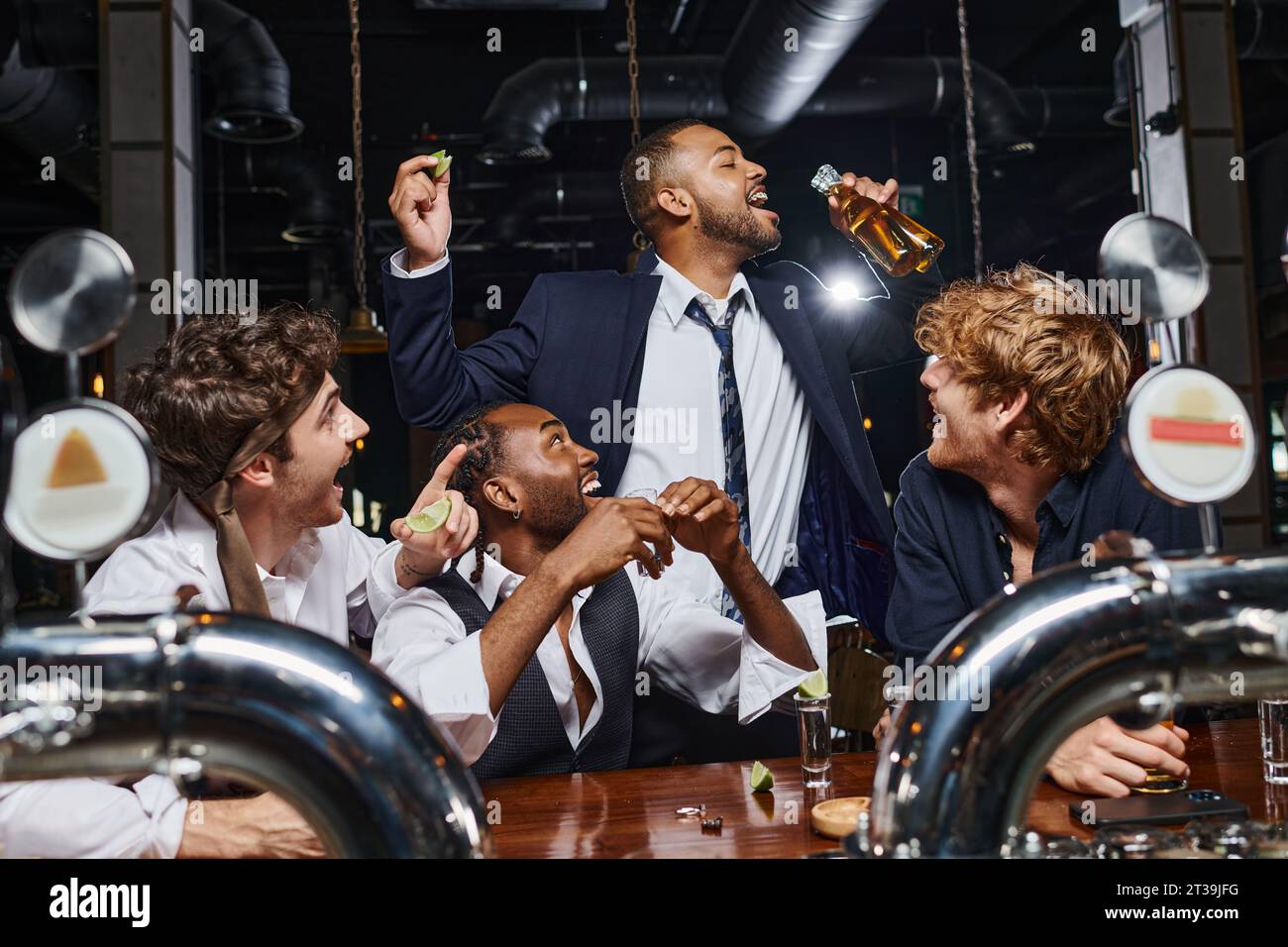 Glückliche Männer, die einen afroamerikanischen Freund sehen, der Bier aus zwei Flaschen trinkt, nachdem er in der Bar gearbeitet hat Stockfoto