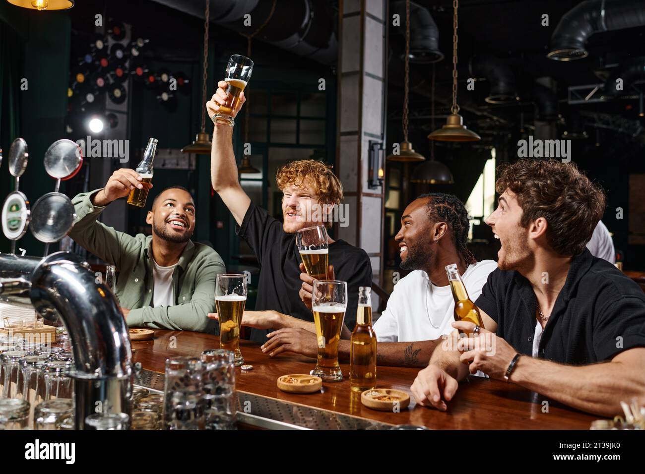 Gruppe von vier glücklichen, multiethnischen männlichen Freunden, die an der Bar ein Glas Bier heben, Junggesellenabschied Stockfoto
