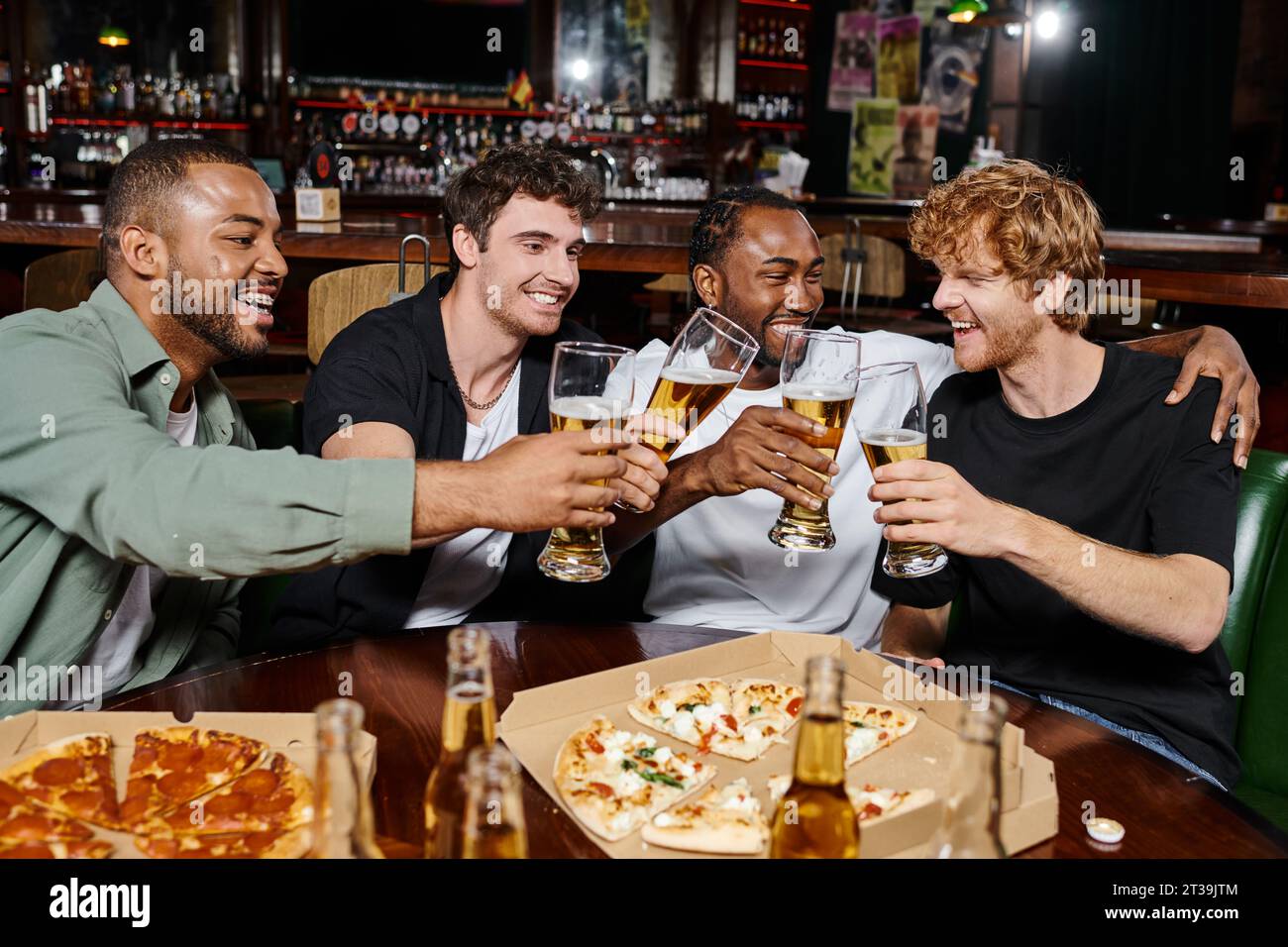 Abends draußen, fröhliche, multiethnische Männer, die in der Bar in der Nähe von einer Pizza Bier trinken, männliche Freundschaft Stockfoto