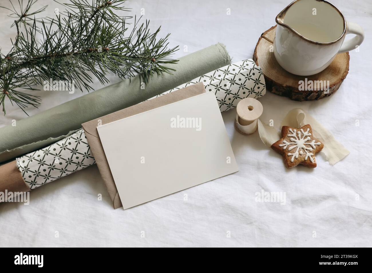 Weihnachtsstillleben. Grußkarte, Einladungsmockup. Lebkuchenkekse, Tannenzweige auf weißem Leinentischtuch. Geschenkpapier mit Stockfoto