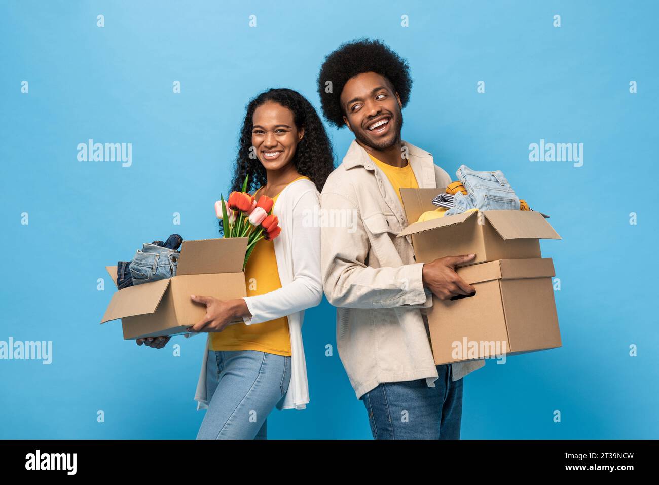 Afro-afro-amerikanisches Paar hält Kästen voller Haushaltssachen in blauer Farbe isolierter Studiohintergrund für Umzugshauskonzept Stockfoto