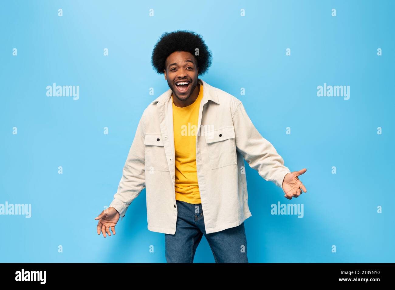 Überraschter afro-amerikanischer Mann lächelt mit geöffneter Hand Geste in hellblauem Farbstudio fotografiert isolierten Hintergrund Stockfoto
