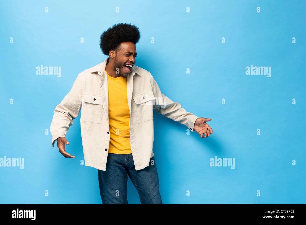 Überraschter afro-amerikanischer Mann lächelt mit geöffneter Hand Geste in hellblauem Farbstudio fotografiert isolierten Hintergrund Stockfoto