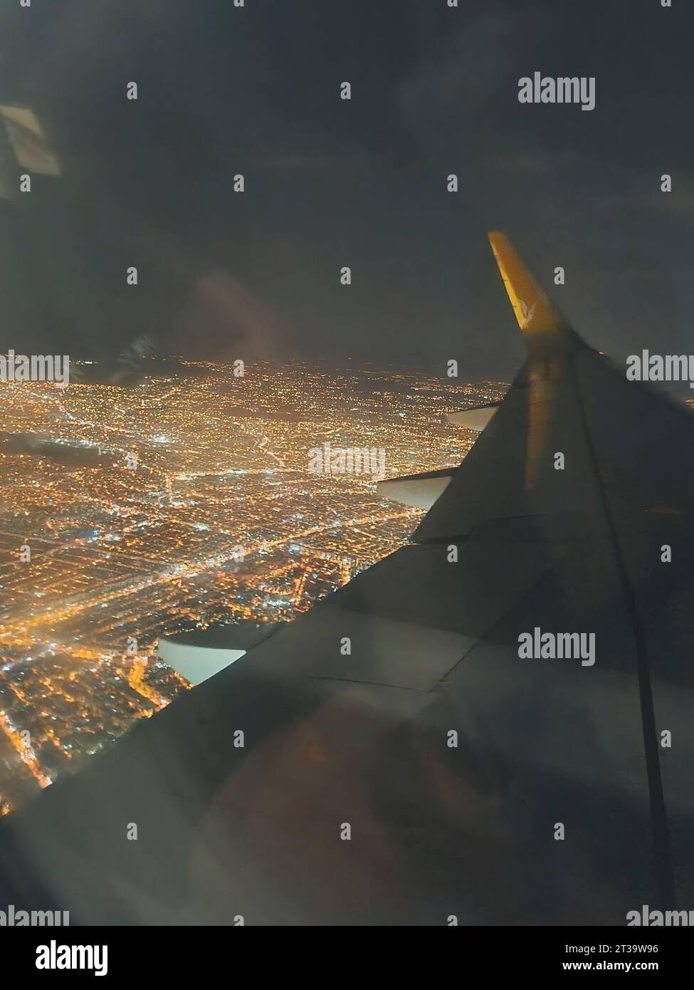 Vertikale Fotoansicht vom Flugzeugfenster zum Flügel und zur Stadt bei Nacht. Weichzeichner. Stockfoto