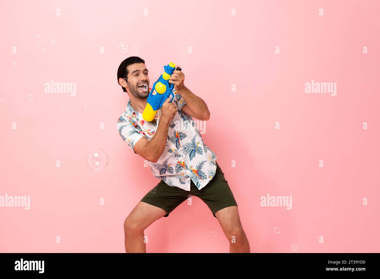 Hübscher, lächelnder junger kaukasischer Touristenmann, der mit einer Wasserpistole im rosafarbenen Studiohintergrund für das Songkran-Festival-Konzept in Thailand und Südosten spielt Stockfoto